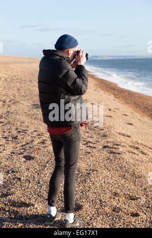 Junger Mann tragen 'Puffa' Jacke und wollene Mütze im Winter mit dem Fotografieren mit einer 35mm Kamera. Stockfoto