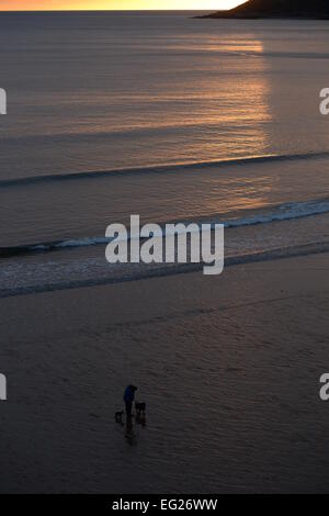 Ein einsamer Wanderer im Caswell Bay genießt die Einsamkeit und Raum von einer leeren Strand bei Sonnenuntergang mit 2 Hunden für Unternehmen auf diesem Gower Strand Stockfoto