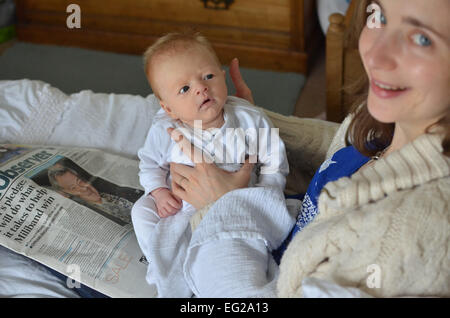 Ein sieben - Wochen altes Baby sitzt auf seiner Mutter Schoß an einem Sonntagmorgen. Stockfoto