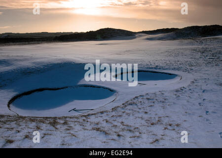 Rechen im Bunker auf dem Schnee bedeckt Links-Golfplatz in Irland bei Sonnenuntergang im verschneiten Winterwetter Stockfoto