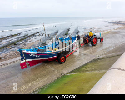 Fischer einen Traktor schleppen sein Boot auf der Helling vom Strand Redcar Cleveland UK, mit seinem Kumpel auf dem Anhänger zu fahren Stockfoto