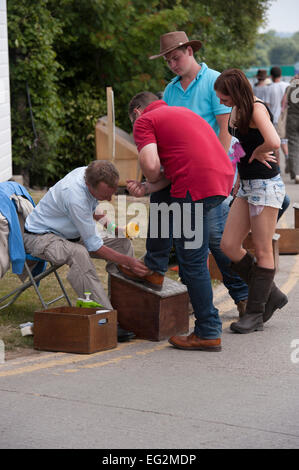 Mann bei der Arbeit als shoeshiner, besetzt Reinigung & Polieren Schuhe der männlichen Besucher Land zeigen als junges Paar watch - Tolle Yorkshire, England, UK. Stockfoto