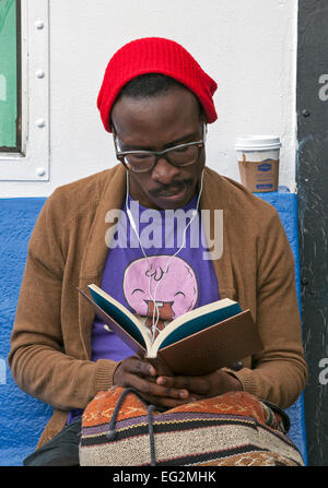 Ein Mann liest ein Buch, während er auf einer Fähre in New York City fährt. Stockfoto