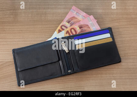 Schwarze Leder-Geldbörse mit Kreditkarten und neue 10 Euro-Scheine auf Holztisch Stockfoto