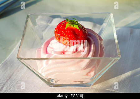 Auf dem Tisch liegt eine Schüssel mit Sahne und Erdbeeren obendrauf. Stockfoto