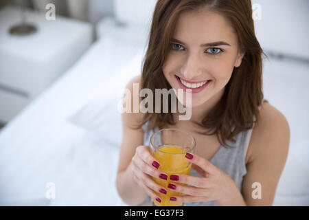 Glückliche Frau trinkt Orangensaft auf dem Bett Stockfoto