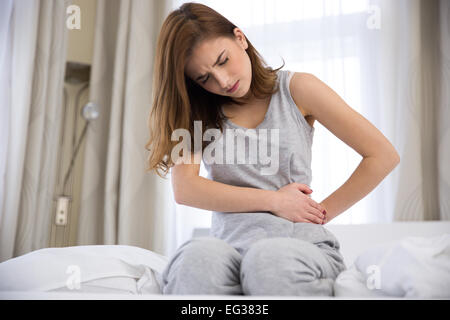 Junge Frau sitzt auf dem Bett mit Schmerzen Stockfoto