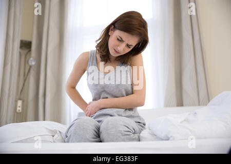 Junge Frau sitzt auf dem Bett mit Schmerzen im Magen Stockfoto