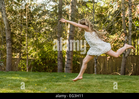 Sieben Jahre altes Mädchen laufen und springen barfuss mit großer Energie und Aufregung in ihrem Hinterhof in Issaquah, Washington, USA Stockfoto