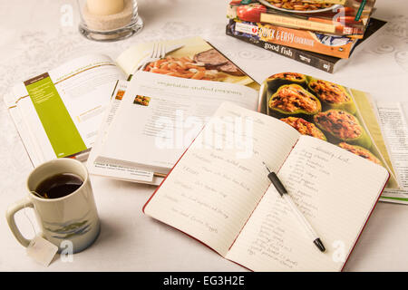Mahlzeit-Planung auf dem Esstisch, mit gesunden Kochbücher verbreiten öffnen.  Ein Notizblock zeigt Tag Abendessen Speisen und Lebensmittel. Stockfoto