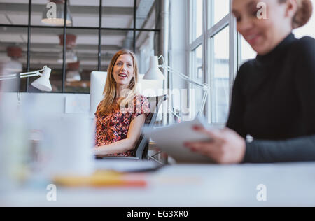Glückliche junge Frau mit einem netten Plausch mit ihrer Kollegin bei der Arbeit Stockfoto
