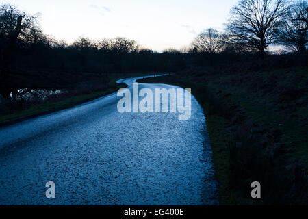Verdrehung kurvenreichen turny Land eisigen feucht nasse Straße in der Dämmerung an einem eiskalten Tag gefährlich & rutschig durch unsichtbare Glatteis gemacht. UK Stockfoto