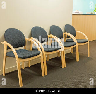 Reihe von leeren Stühlen, modernen Stil, geschwungene Holzrahmen & blau / grau Polster gegen weiße Wand im Wartezimmer des Arztes Stockfoto