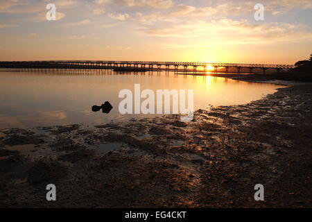 Bild vom Sonnenuntergang am Fluss mit Holzbrücke am Horizont. Gefangen in Algarve, Portugal Stockfoto