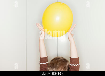 Kind hält gelben Ballon mit erhobenen Armen über den Kopf. Lustige Kindheit Moment. Stockfoto