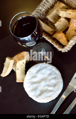 Teller mit Käse und ein Glas Rotwein auf dem Tisch Stockfoto