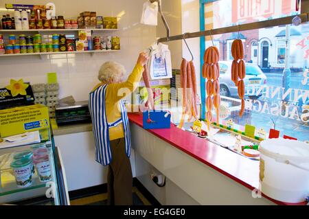 Alte Frau messen, Cumberland Würstchen in einem traditionellen Metzger-Shop gekühlt Zähler. Stockfoto