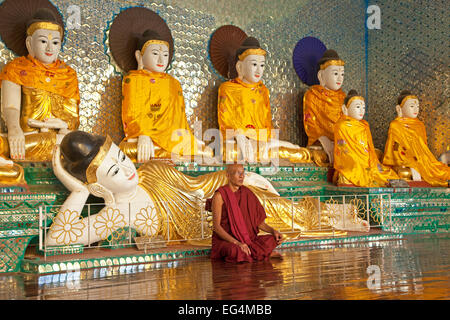 Buddhistischer Mönch betend vor Buddha-Statuen in der Shwedagon Zedi Daw-Pagode in Yangon / Rangun, Myanmar / Burma Stockfoto