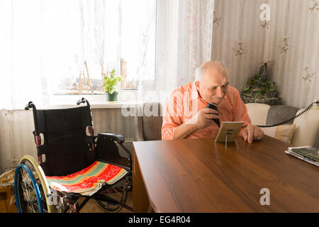 Älterer Mann rasieren Bärte mit Elektrorasierer an das Wohnzimmer mit seinem Rollstuhl auf der Seite sitzen. Stockfoto