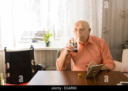 Nahaufnahme sitzen alte Glatzkopf in orange Shirt hält eine Flasche Spray Aftershave nach der Reinigung sein Gesicht im Wohnzimmer. Stockfoto