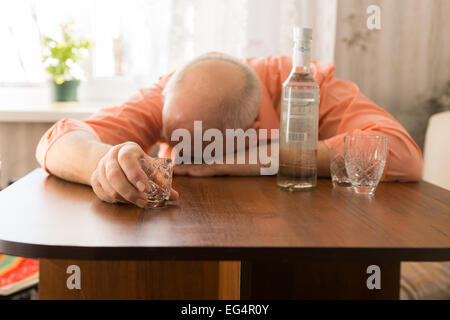 Nahaufnahme betrunken alten kahlen Mann stützte sich auf den Holztisch mit Wodka Holding ein kleines Glas Stockfoto