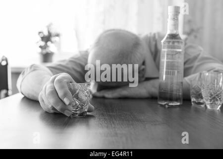 Nahaufnahme betrunken Greis schlafen auf dem Tisch mit dem Wein zu halten, während ein kleines Glas. In Monochrom erfasst. Stockfoto