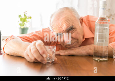 Schließen Sie betrunken ältere halten kleine Shot Glas am Holztisch mit Wodka, während in die Kamera schaut. Stockfoto