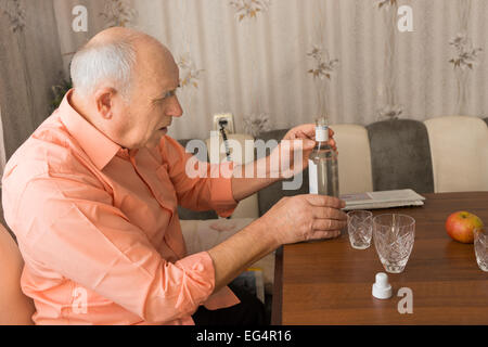 Nahaufnahme Seitenansicht eine ernsthafte Greis hält eine Flasche Vodka Wein auf dem Holztisch Stockfoto