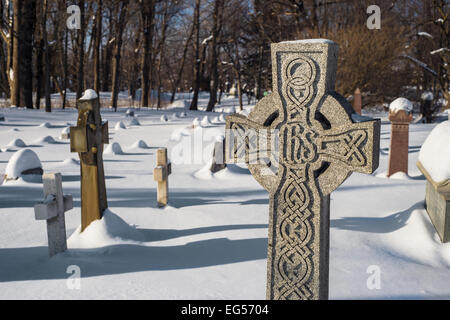 Grabsteine, die unter dem Schnee in einem amerikanischen Friedhof mit einem Kreuz im Vordergrund Stockfoto