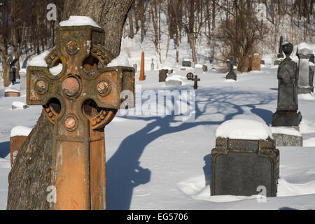 Grabsteine, die unter dem Schnee in einem amerikanischen Friedhof mit einem Kreuz im Vordergrund Stockfoto