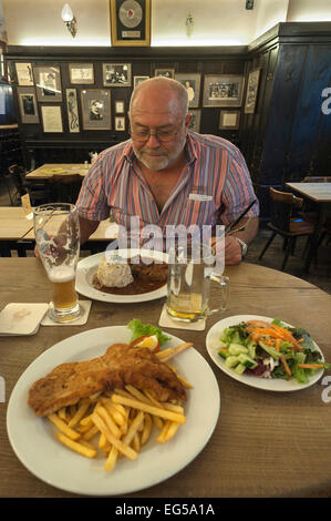 Älterer Mann sitzt vor einer herzhaften Mahlzeit, an der Vorderseite einen Teller mit Schnitzel mit Pommes in einem bayrischen Restaurant, München Stockfoto