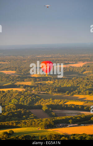 Red Hot Air Balloon und Schirm über ländliche Landschaft fliegen hängen, South Oxfordshire, England Stockfoto