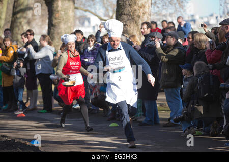 Westminster, London, UK. 17. Februar 2015. Mitglieder des Parlaments David Burrows MP (Enfield, Southgate) führt parlamentarische Pressekorps Sophie Ridge (Sky News) in die jährliche Faschingsdienstag parlamentarischen Pancake Race auf Victoria Tower Gardens in Westminster, London, UK-Credit: Jeff Gilbert/Alamy Live News Stockfoto