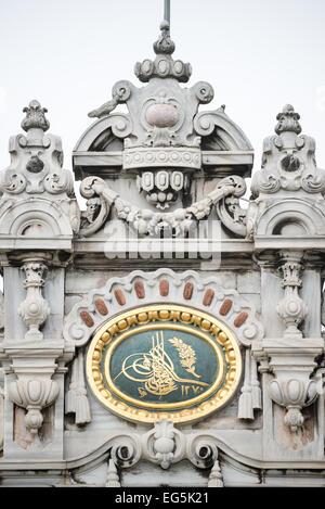 Dolmabahçe-Palast Ottomanische Tughra Detail Istanbul Türkei | ISTANBUL — Eine kunstvolle osmanische Tughra, das kalligraphische Monogramm des Sultans, ist in vergoldeter Reliefarbeit auf einem Marmorpfeiler des Dolmabahçe-Palastes eingemeißelt. Die Tughra diente als kaiserliches Siegel der Souveränität, gestempelt auf Dekreten, Münzen und Gebäuden im gesamten Reich; dieses Exemplar ist in osmanischen Ziffern auf das islamische Jahr 1270, etwa 1854, datiert. Die Barock- und Rokoko-Schnitzereien des Palastes umgeben es in Marmorranken und Blumengirlanden. Stockfoto