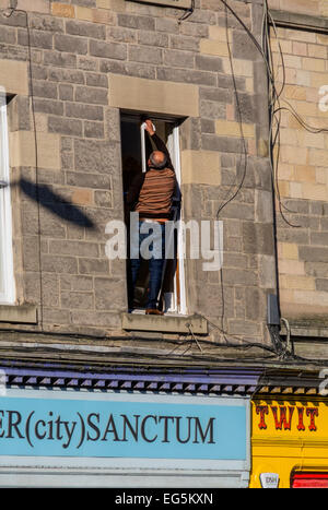 Fensterputzen ohne Verwendung einer Leiter - hat dieser Mann duckte sich auf ersten Stock Fensterbrett stehen. Stockfoto