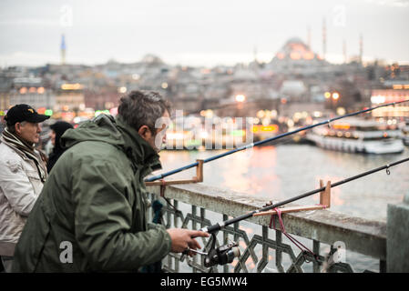 ISTANBUL, Türkei / Türkiye — Fischer säumen den Rand der Galata-Brücke mit ihren Linien über die Seite zum Goldenen Horn. Die Galata-Brücke, die das Goldene Horn überspannt und Eminonu mit Karakoy verbindet, ist eine zweistöckige Brücke, die Straßen-, Straßenbahn- und Fußgängerverkehr auf der obersten Ebene mit Restaurants und Bars auf der darunter liegenden Ebene abwickelt. In der Ferne befindet sich die Suleymaniye-Moschee. Stockfoto