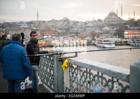 ISTANBUL, Türkei / Türkiye — Fischer säumen den Rand der Galata-Brücke mit ihren Linien über die Seite zum Goldenen Horn. Die Galata-Brücke, die das Goldene Horn überspannt und Eminonu mit Karakoy verbindet, ist eine zweistöckige Brücke, die Straßen-, Straßenbahn- und Fußgängerverkehr auf der obersten Ebene mit Restaurants und Bars auf der darunter liegenden Ebene abwickelt. In der Ferne befindet sich die Suleymaniye-Moschee. Stockfoto