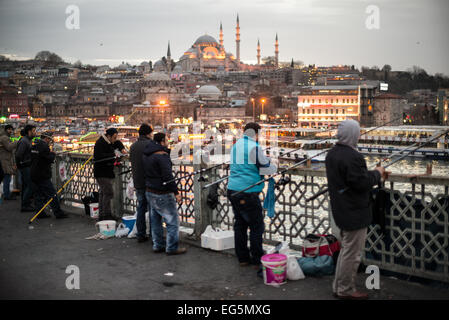 ISTANBUL, Türkei / Türkiye — Fischer säumen den Rand der Galata-Brücke mit ihren Linien über die Seite zum Goldenen Horn. Die Galata-Brücke, die das Goldene Horn überspannt und Eminonu mit Karakoy verbindet, ist eine zweistöckige Brücke, die Straßen-, Straßenbahn- und Fußgängerverkehr auf der obersten Ebene mit Restaurants und Bars auf der darunter liegenden Ebene abwickelt. In der Ferne befindet sich die Suleymaniye-Moschee. Stockfoto