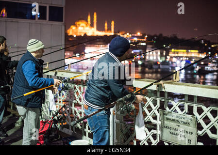 ISTANBUL, Türkei / Türkiye — Fischer säumen den Rand der Galata-Brücke mit ihren Linien über die Seite zum Goldenen Horn. Die Galata-Brücke, die das Goldene Horn überspannt und Eminonu mit Karakoy verbindet, ist eine zweistöckige Brücke, die Straßen-, Straßenbahn- und Fußgängerverkehr auf der obersten Ebene mit Restaurants und Bars auf der darunter liegenden Ebene abwickelt. Stockfoto