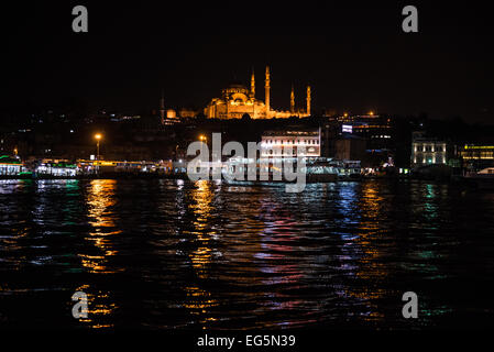 ISTANBUL, Türkei / Türkiye – Ein nächtlicher Blick auf die Suleymaniye-Moschee von der Galata-Brücke. Die Galata-Brücke, die das Goldene Horn überspannt und Eminonu mit Karakoy verbindet, ist eine zweistöckige Brücke, die Straßen-, Straßenbahn- und Fußgängerverkehr auf der obersten Ebene mit Restaurants und Bars auf der darunter liegenden Ebene abwickelt. Stockfoto