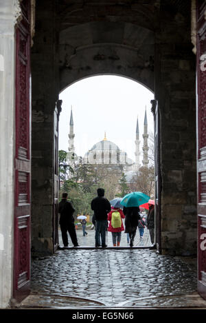 Besucher kommen und gehen im Regen durch die kaiserlichen Tor (Bâb-ı Hümâyûn) am Topkapi-Palast, mit Tne Eingang einrahmen der blauen Moschee in der Ferne. Auf einer Halbinsel mit Blick auf den Bosporus und das Goldene Horn war Topkapi-Palast der Hauptwohnsitz der osmanischen Sultane seit etwa 400 Jahren (1465 – 1856) ihrer 624-Jahr-Herrschaft über Konstantinopel und das Osmanische Reich. Heute ist es eine der wichtigsten Sehenswürdigkeiten Istanbuls. Stockfoto