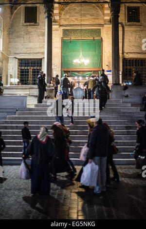 Yeni Camii Eingangstreppe Nacht Istanbul Türkei | ISTANBUL, Türkei — Die Eingangstreppe der Yeni Camii (Neuen Moschee) ist nachts im Bezirk Eminönü beleuchtet. Der Bau begann 1597 unter Valide Sultan Safiye Sultan und wurde 1663 unter Hatice Turhan Valide Sultan nach einer Verzögerung von mehr als einem halben Jahrhundert abgeschlossen, wobei das gesamte Komplex am 30. Oktober 1665 eingeweiht wurde — was sie zur letzten großen kaiserlichen Moschee der klassischen osmanischen Zeit macht. Der Komplex umfasst die Hauptmoschee mit ihrer zentralen Kuppel und vier Halbkuppeln, den angrenzenden Gewürzbasar, der errichtet wurde, um ihre Stiftung zu finanzieren Stockfoto