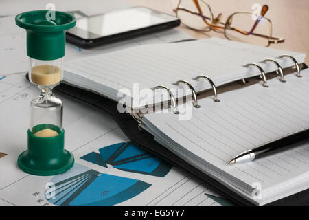 Sanduhr, Tagebuch, Stift, Gläser und Telefon, liegend auf einem Hintergrund von Diagrammen und Graphen Stockfoto