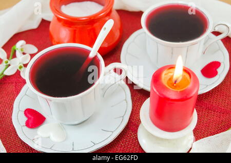 Zwei Vintage Tassen Hibiskustee dekoriert mit Herzen und eine brennende Kerze Stockfoto