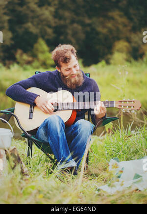 lächelnder Mann mit Gitarre und Dixie im camping Stockfoto