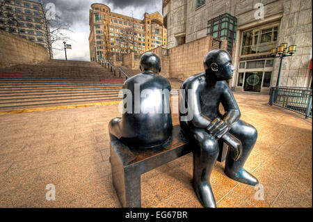 schwarze farbige Skulptur von zwei Menschen sitzen auf einer Bank am Canary wharf Stockfoto