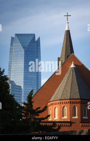 Aus der richtigen Perspektive betrachtet, der Kirchturm und das Kreuz einer kleinen Kirche erhebt sich gegen höchste Gebäude in der Stadt. Stockfoto