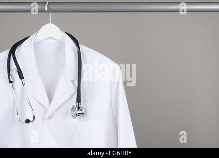Ein Arzt Kittel und Stethoskop auf Kleiderbügel vor einem grauen Hintergrund. Closeup auf einem weißen Bügel mit einem grauen Hintergrund in hor Stockfoto