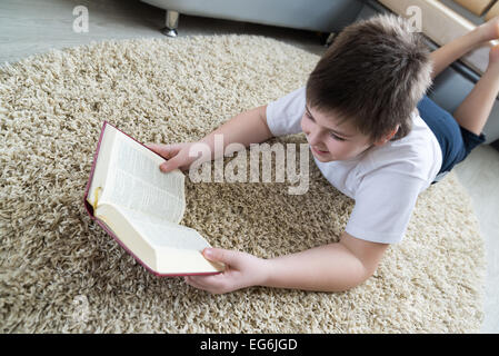 Junge liest ein Buch auf dem Teppich im Zimmer Stockfoto