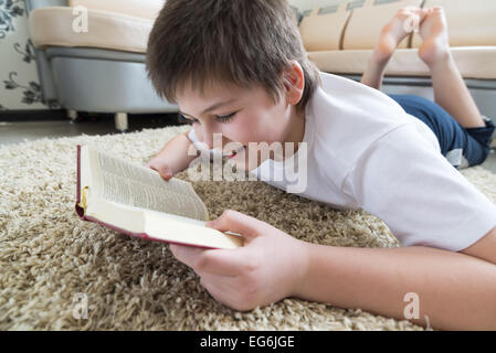 Junge liest ein Buch auf dem Teppich im Zimmer Stockfoto